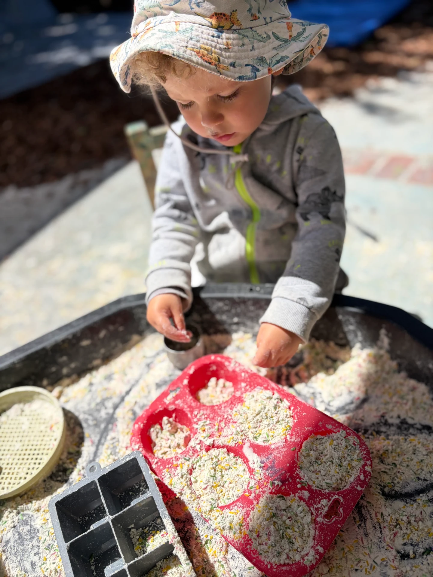 A toddler in a sun hat exploring a sensory tray in the nursery