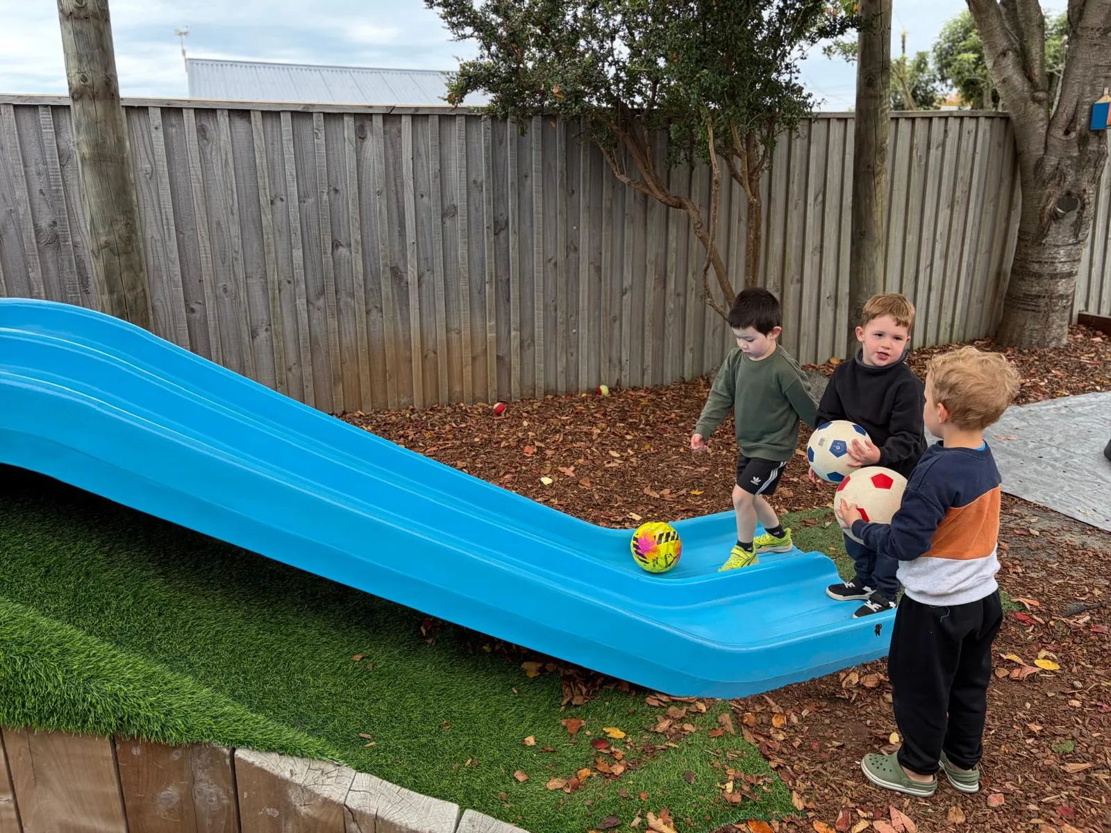 Three preschoolers with soccer balls beside the slide