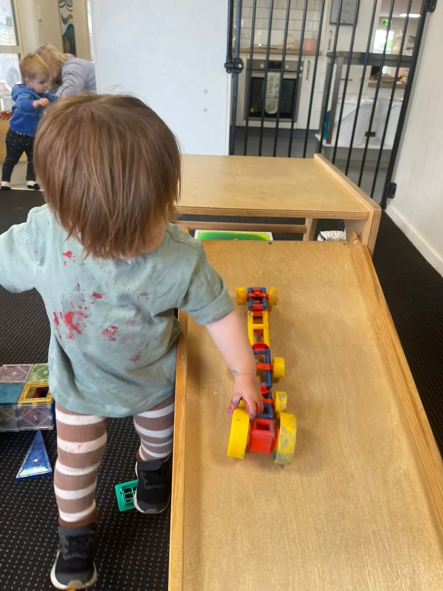 A toddler rolling a wooden car down a ramp indoors