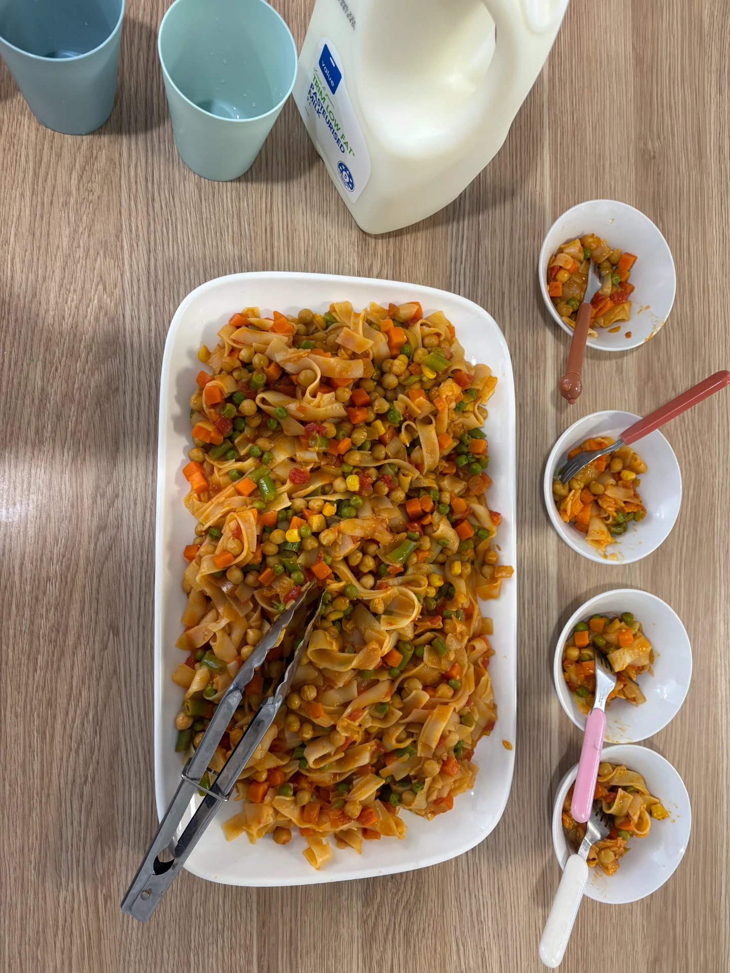 A platter of pasta with vegetables and chickpeas beside small bowls served for tamariki
