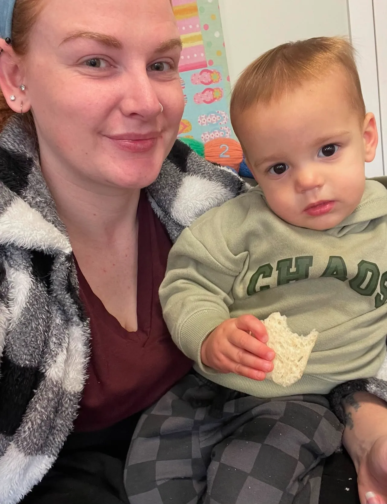 A kaiako and a baby holding a piece of toast, sitting together on the mat