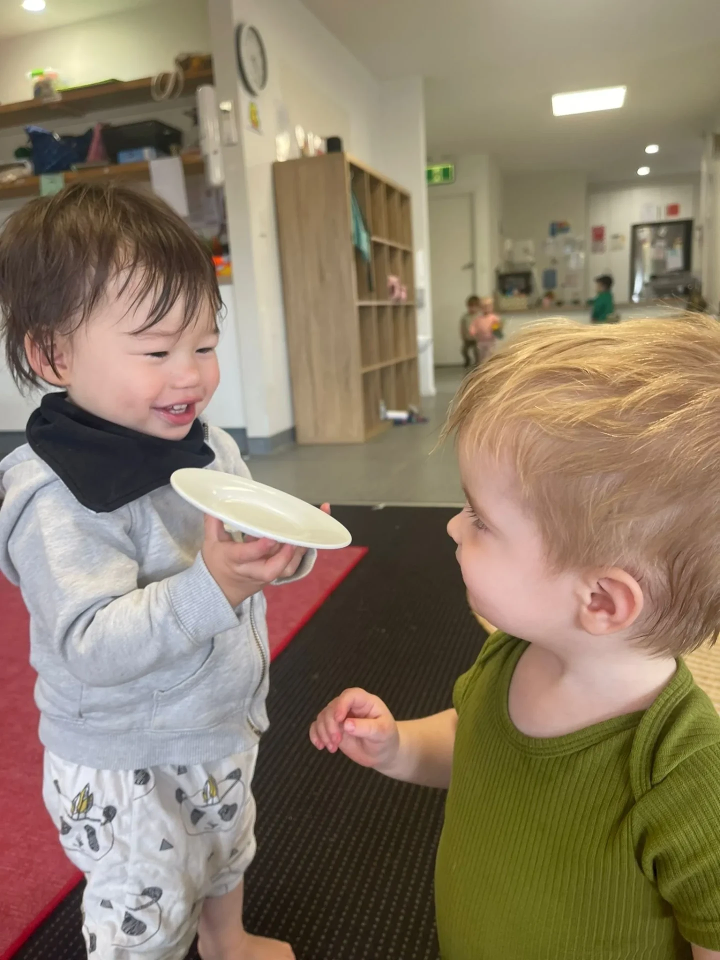 Two toddlers laughing together while sharing a plate indoors