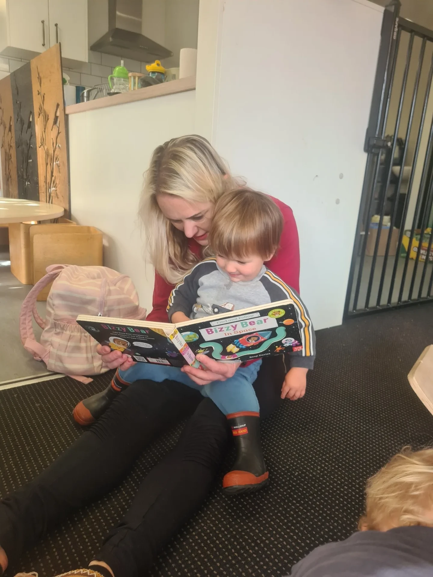 A Wonderhub kaiako sitting on the floor reading a picture book with a toddler
