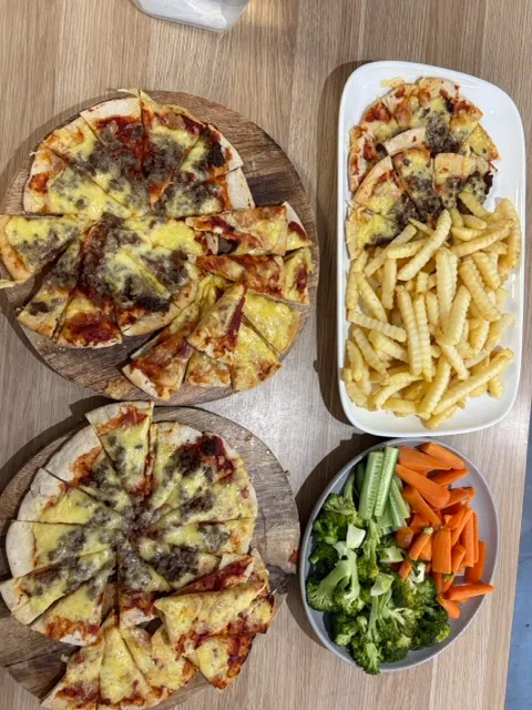 Home made pizzas cut into slices with oven fries and a bowl of broccoli, carrot and celery