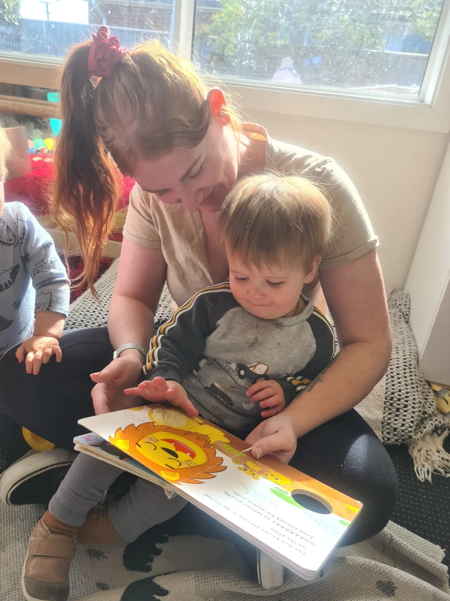 A Wonderhub kaiako reading a picture book with a toddler on her lap
