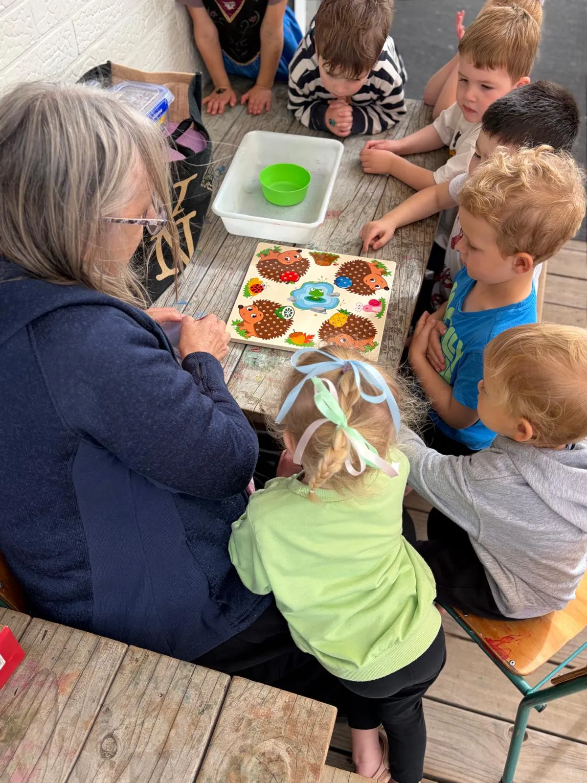 A kaiako working through a puzzle with a group of preschoolers at the outdoor table