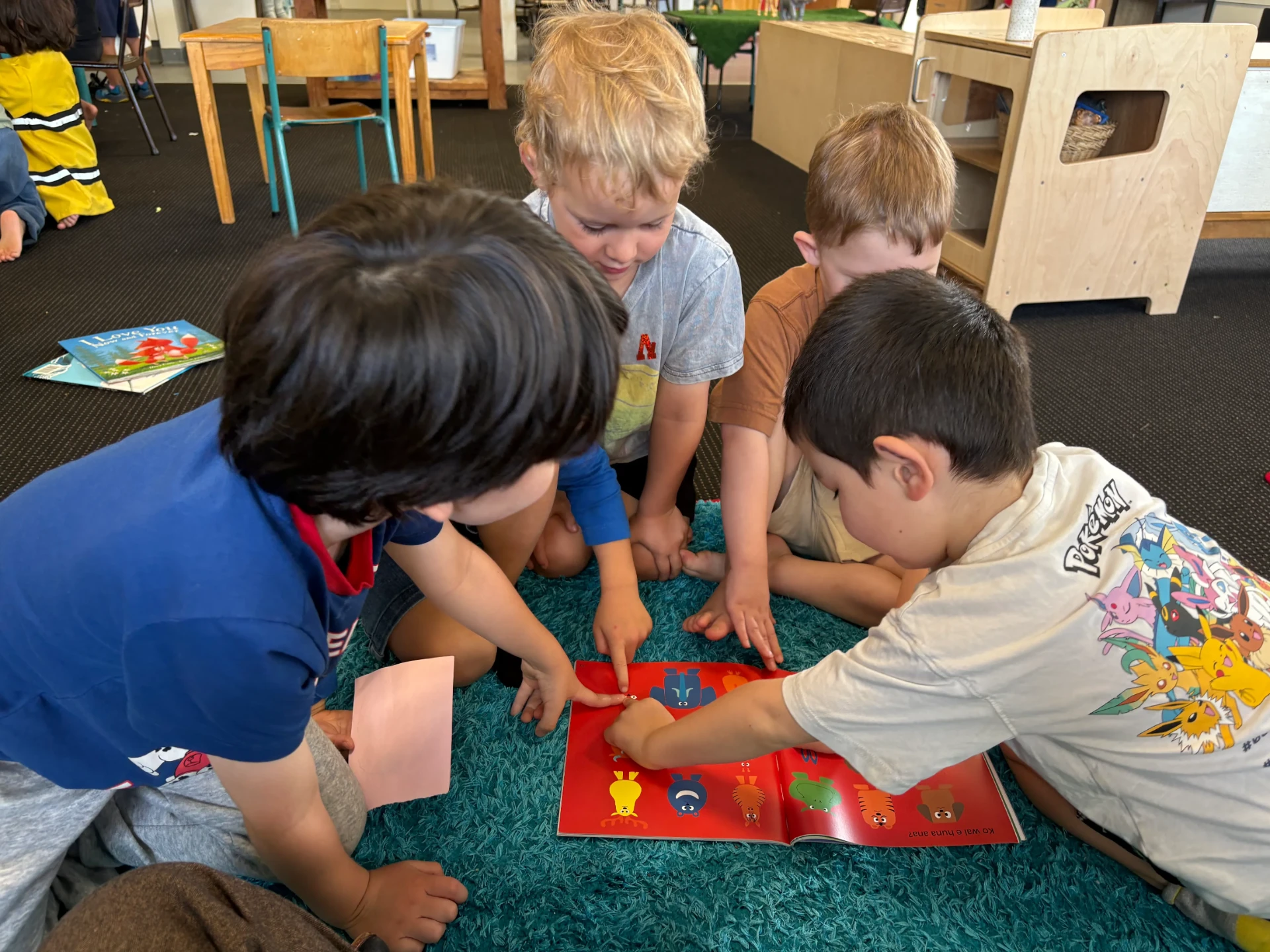 Four tamariki gathered around an open picture book on the mat indoors