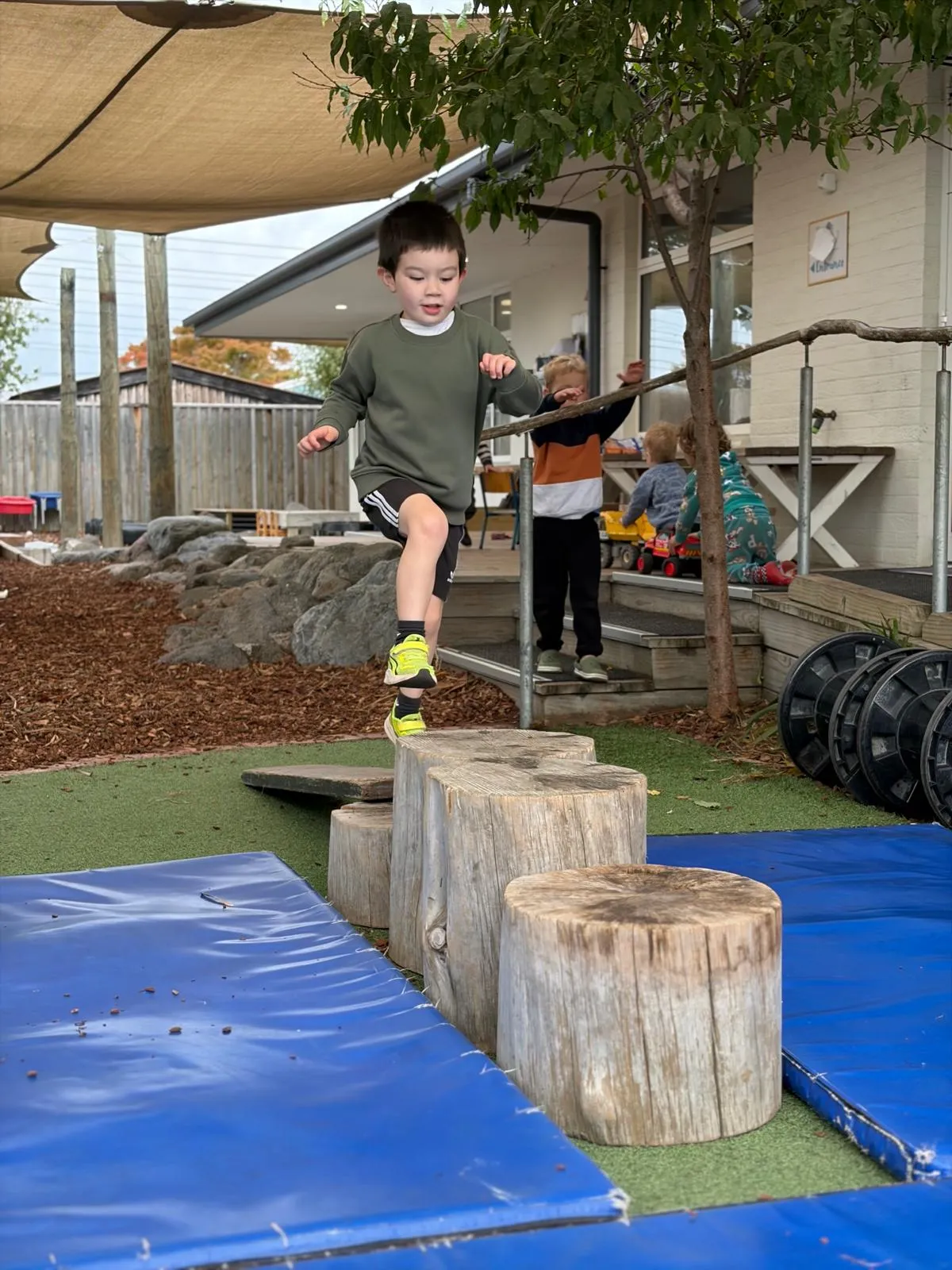 A preschooler leaping between wooden log stumps in the playground