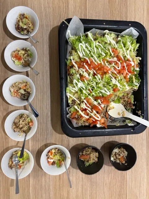 A tray of nachos with lettuce, tomato and yoghurt dressing portioned into small bowls