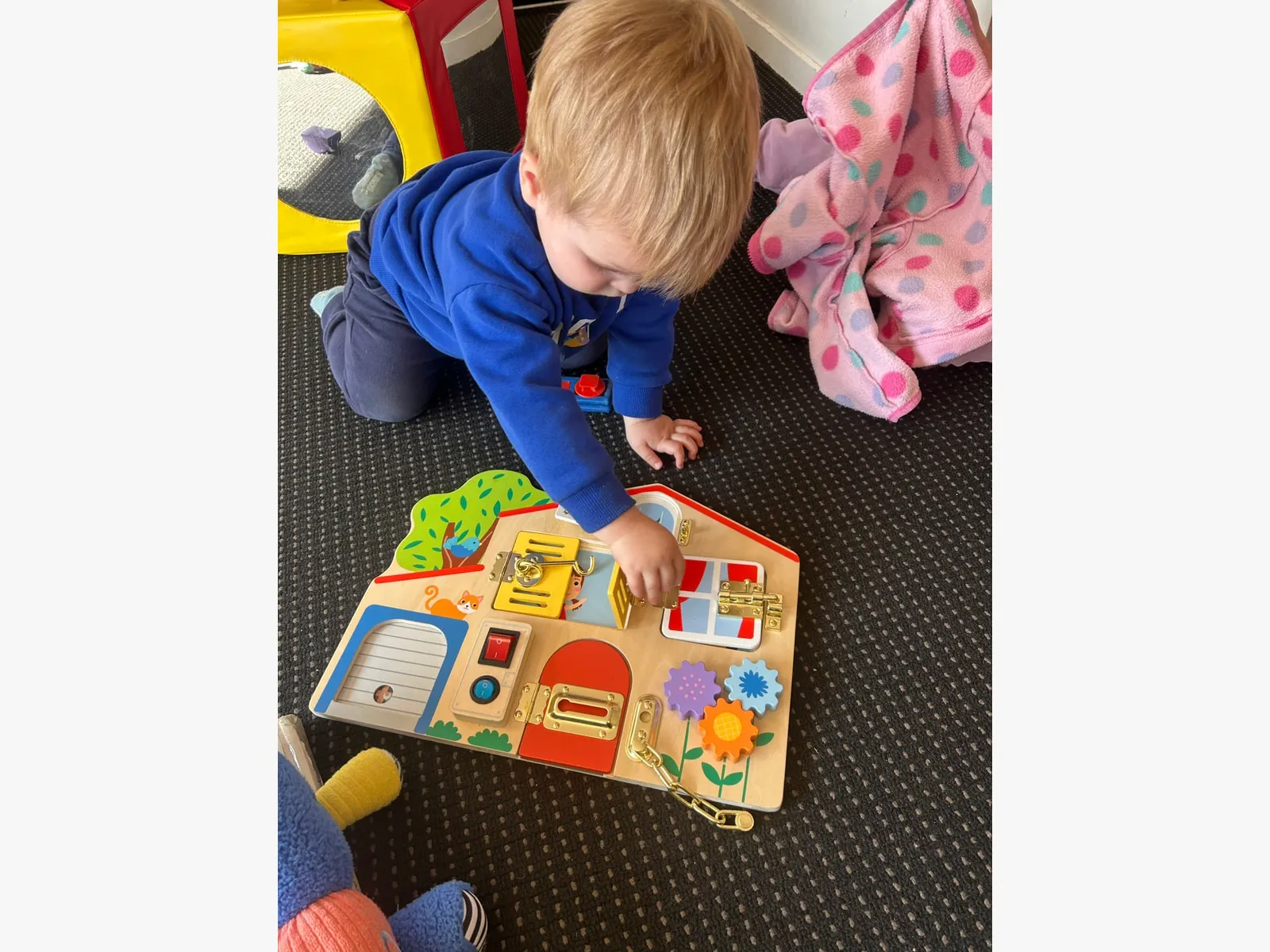 A toddler exploring latches and locks on a wooden activity board