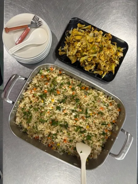 A tray of vegetable fried rice with roasted cauliflower, plates and serving spoons ready