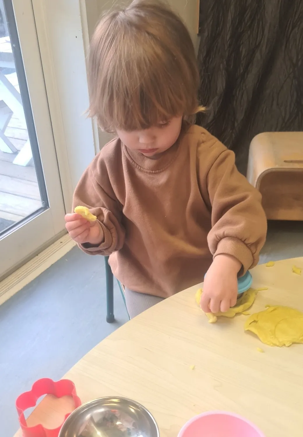 A toddler pressing cutters into yellow playdough at the table