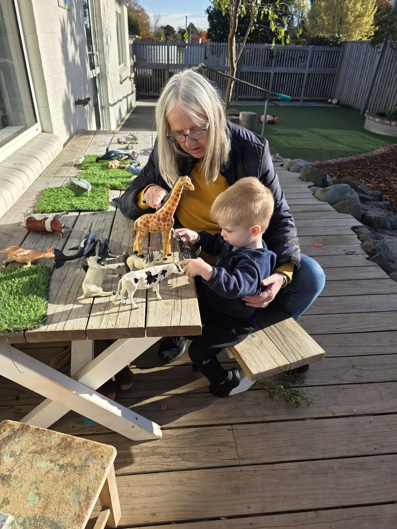A kaiako and toddler playing with animal figures on the deck outside