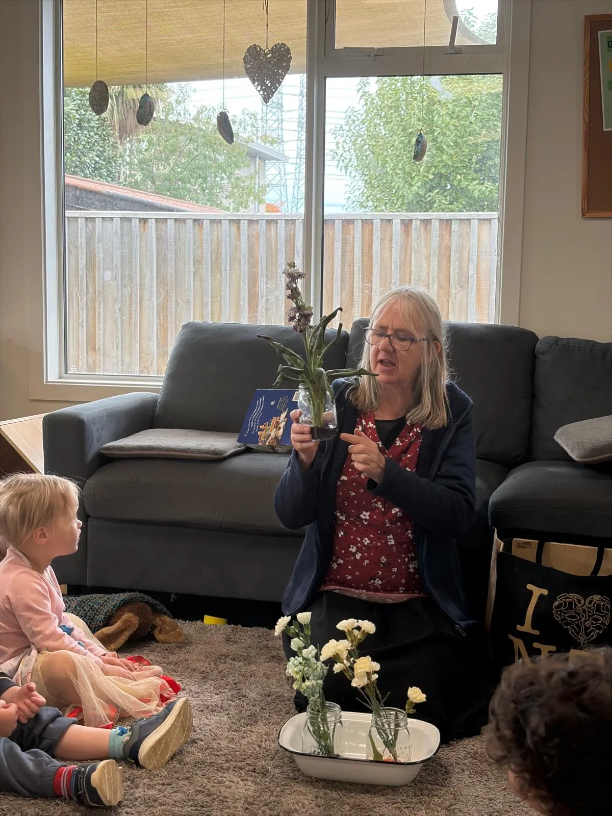 A kaiako showing tamariki fresh flowers and leaves during mat time in the lounge
