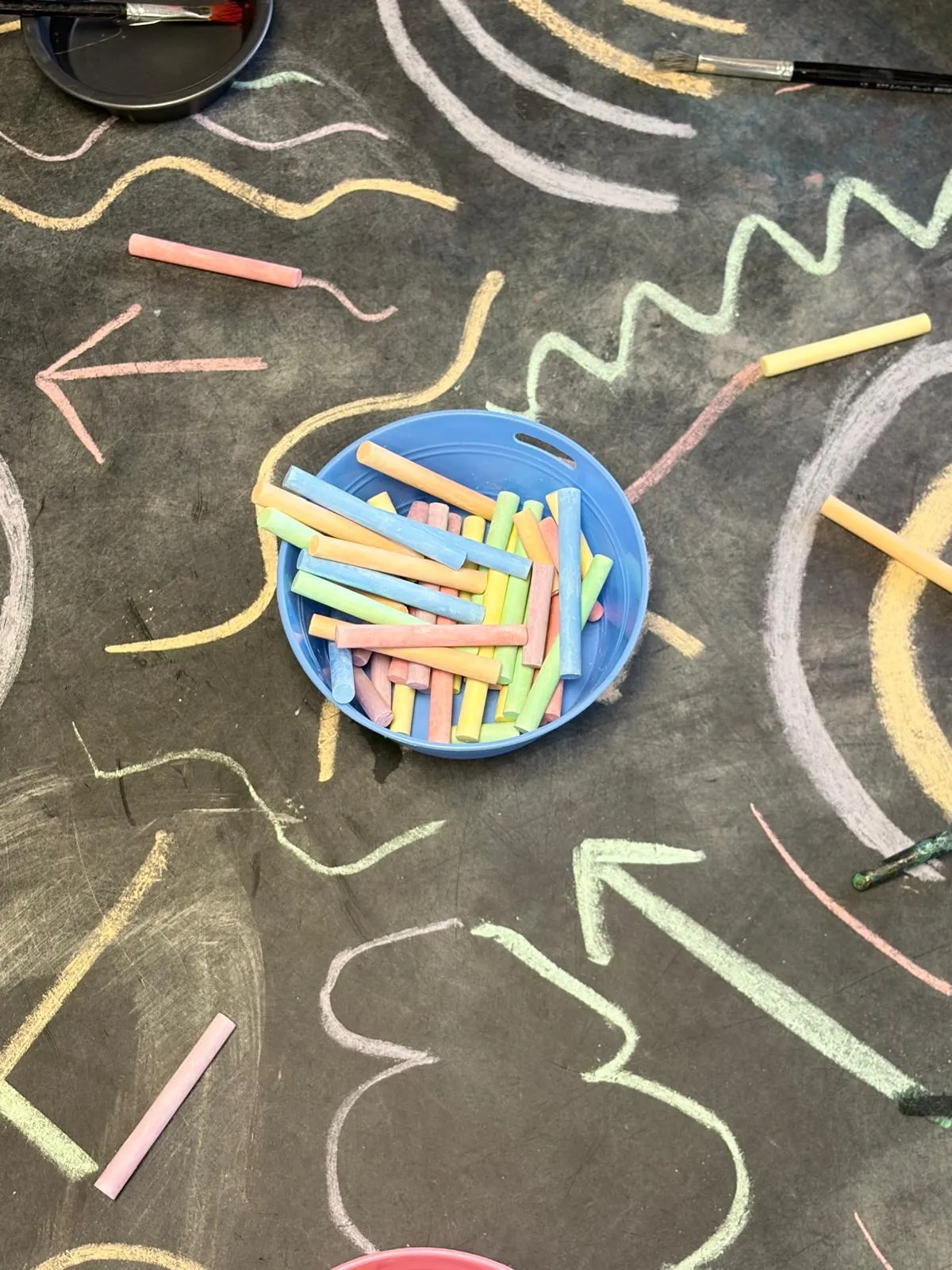 Chalk drawings and a tray of coloured chalk on the outdoor blackboard