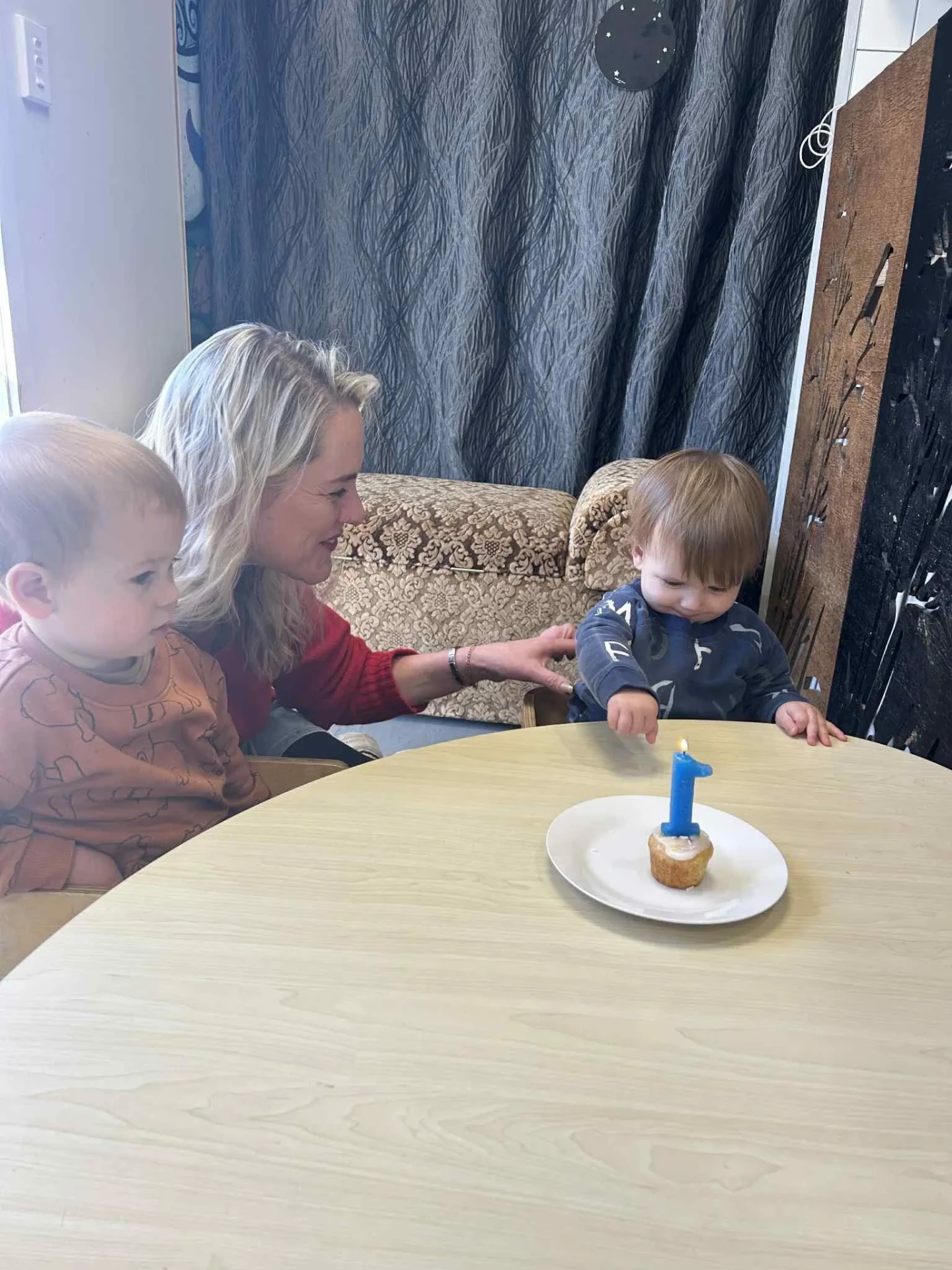 A kaiako helping two toddlers celebrate a first birthday with a candle