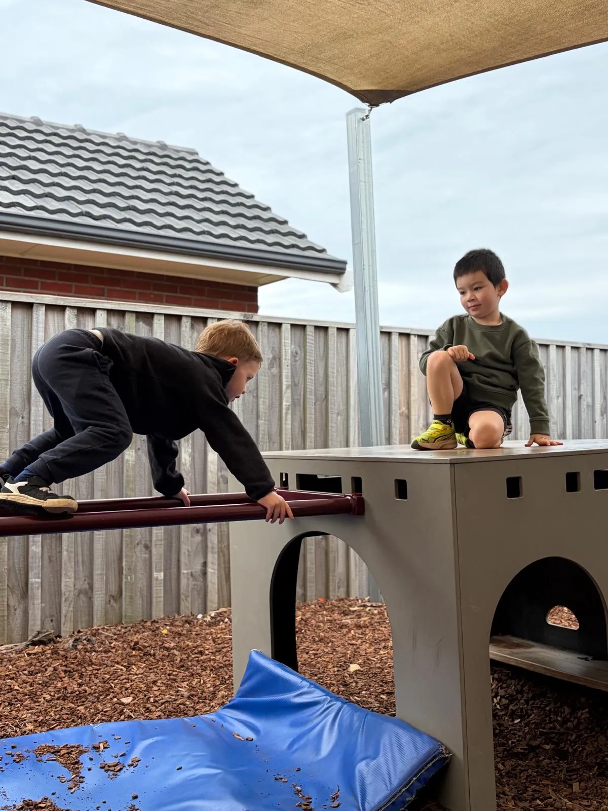 Two tamariki climbing on the outdoor platform under the shade sail